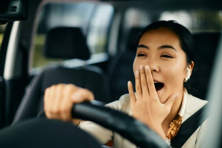 Tired woman yawning while driving a car.