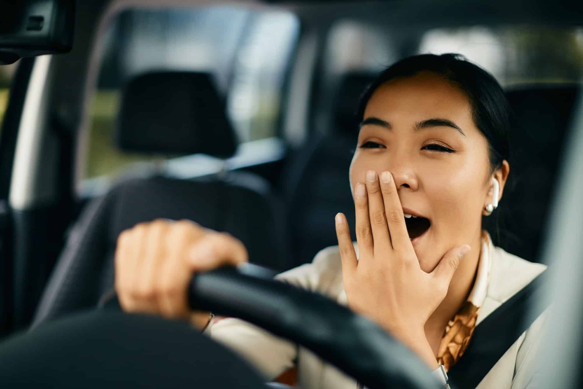 Tired woman yawning while driving a car.